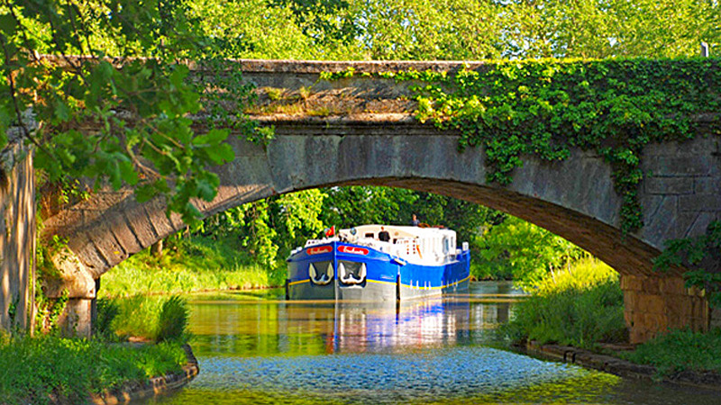 Hotel Barge Enchante approaching a pretty bridge while cruising on the Canal du Midi in the south of France