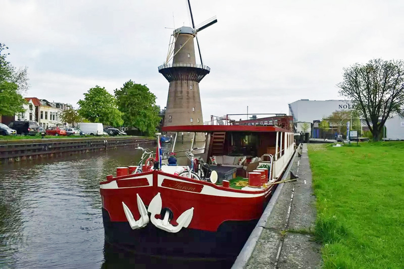 Hotel Barge Aurora moored on the bank of canal near a windmill