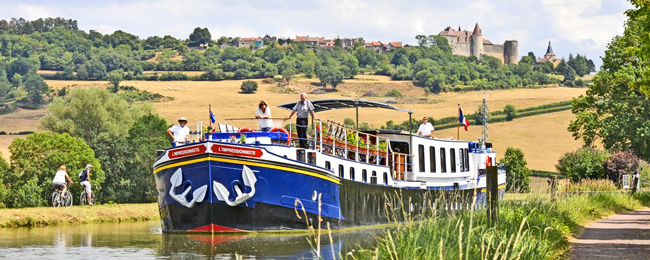 French Hotel Barge L'Impressionniste gliding along the Canal de Bourgogne with Châteauneuf in the background