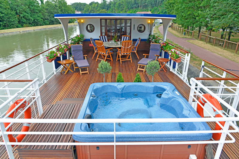 French Hotel Barge Renaissance - Overview of sundeck with tables & chairs, sun loungers, hot tub / spa pool, and flower boxes