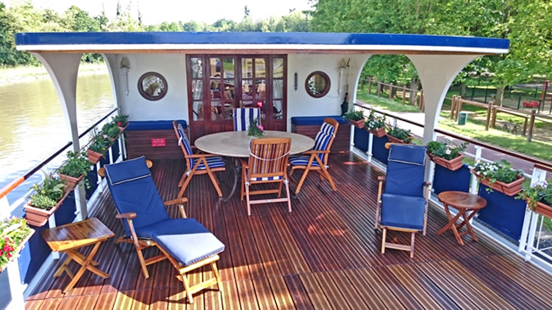 French Hotel Barge Renaissance - Shaded section of the sundeck with tables & chairs, sun loungers, and flower boxes
