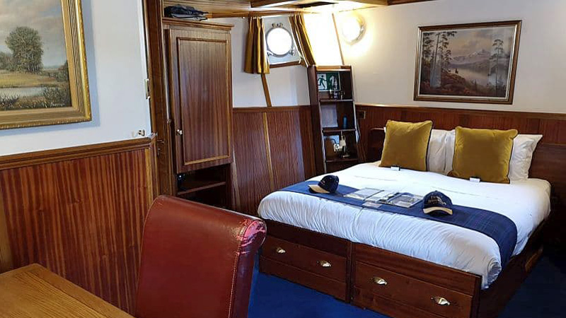 Scottish Hotel Barge Scottish Highlander - The Cameron Suite is the largest guest cabin. This photo shows the double berth, paintings, cupboard, desk & chair