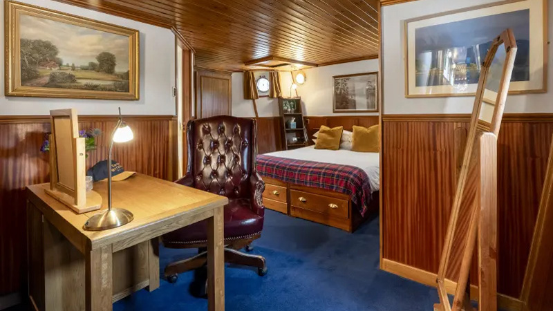 Scottish Hotel Barge Scottish Highlander - The Cameron Suite is the largest guest cabin. This photo is another view showing paintings on wall, desk with comforable chair, and full length mirror with double berth in the background