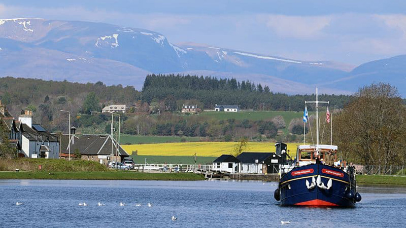 Scottish Hotel Barge Scottish Highlander cruising past farms with the Highlands in the background