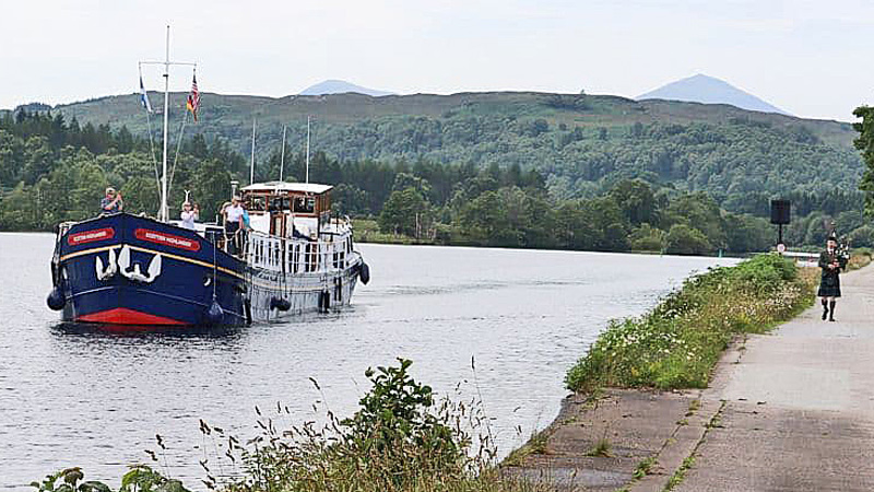 Scottish Hotel Barge Scottish Highlander with a man playing bagpipes on the shore