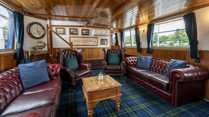 Scottish Hotel Barge Scottish Highlander - Saloon with leather Chesterfield sofas and armchairs, tartan flooring, brass fixtures