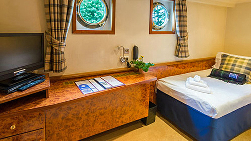Scottish Hotel Barge Spirit of Scotland - Guest cabin with double bed arrangement. Photo shows bed, TV, table, portholes, drawers, and counterspace