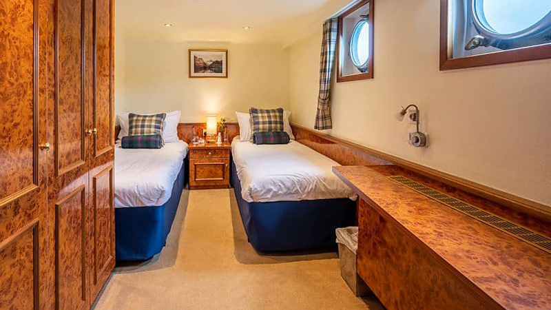 Scottish Hotel Barge Spirit of Scotland - Guest cabin with twin bed arrangement. Photo shows beds, bedside table, portholes, closets, and counterspace